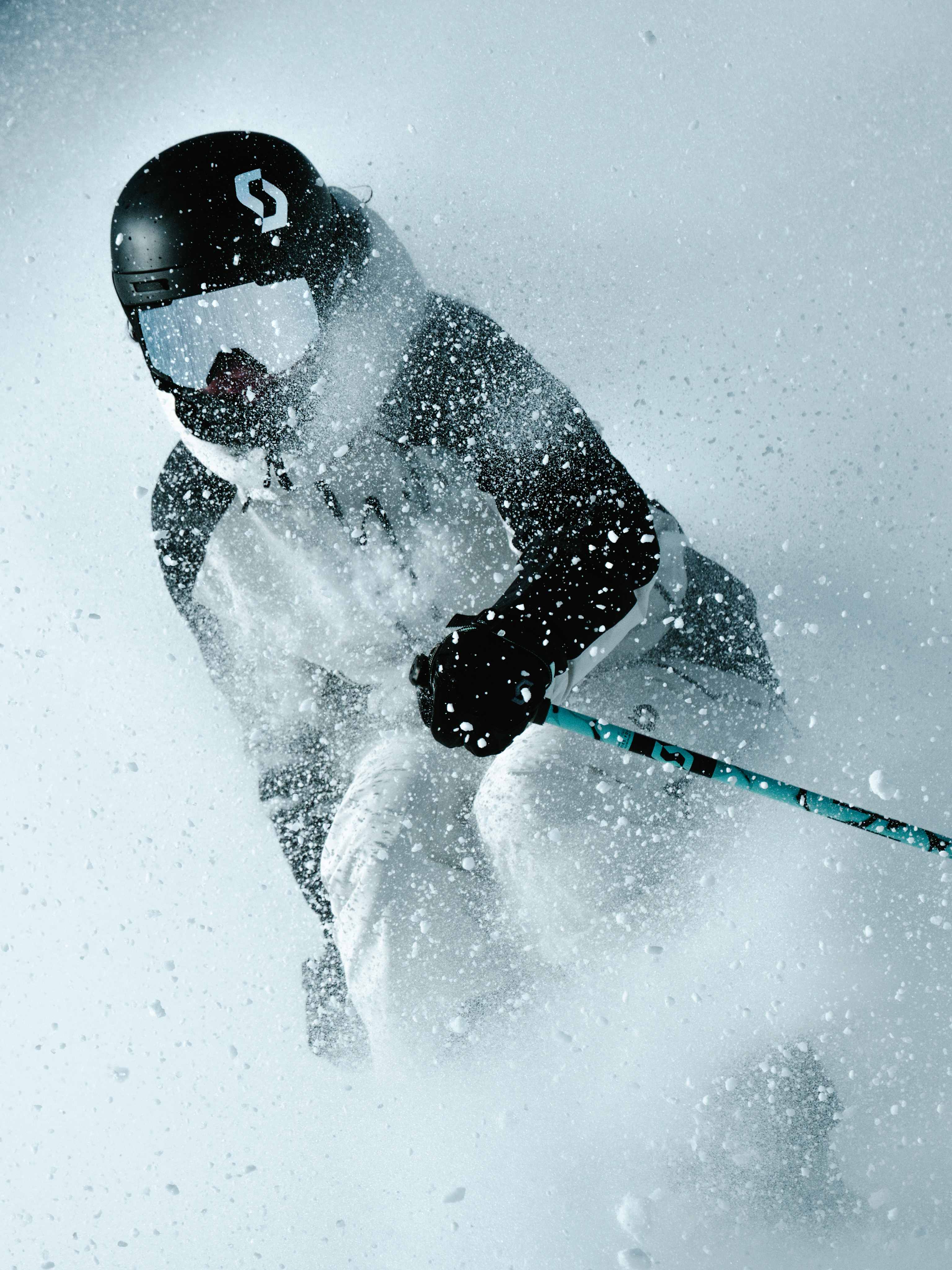 A skier in a black helmet and white snow gear carves through a cloud of snow against a bright, blurred background.