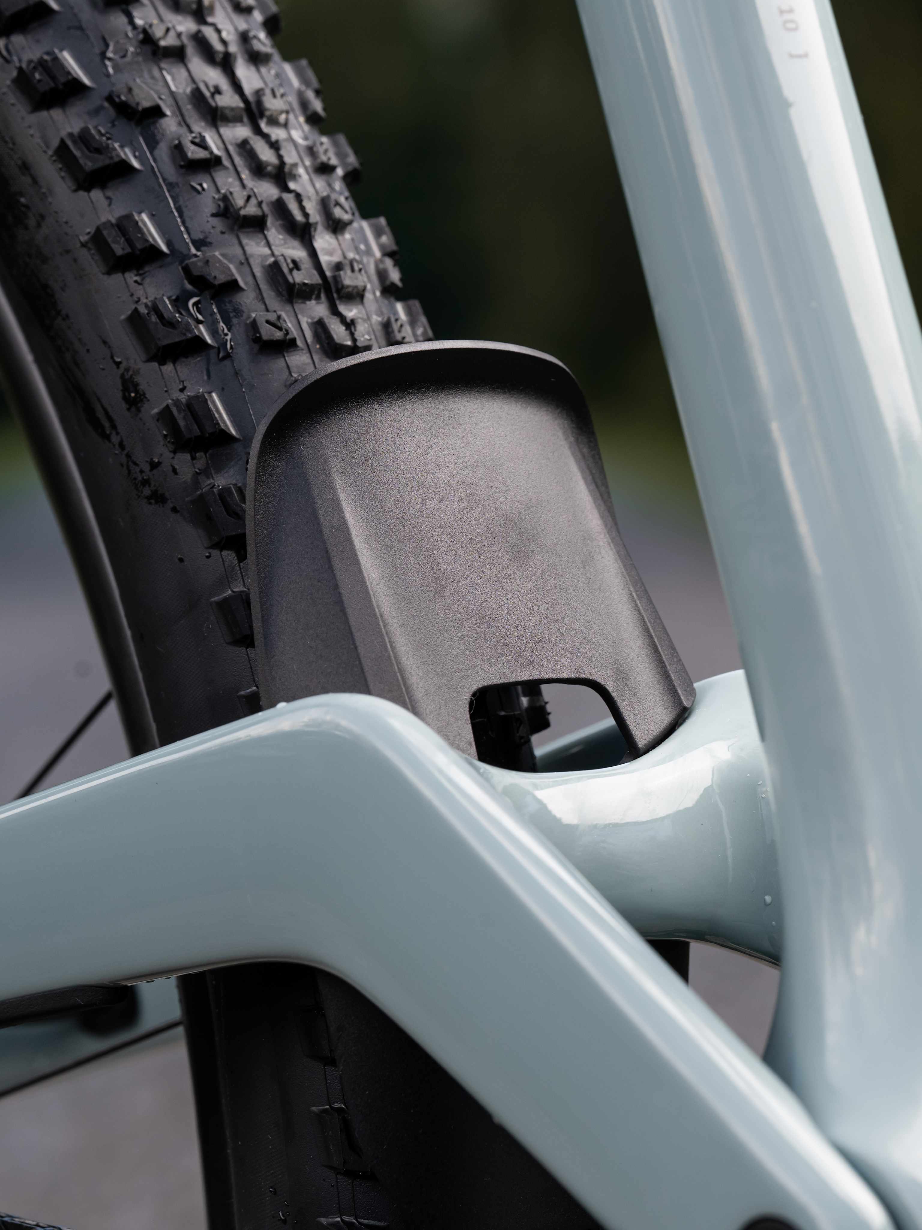 A close-up of a light blue bicycle frame in the foreground is set against a blurred background of trees and a dirt path.