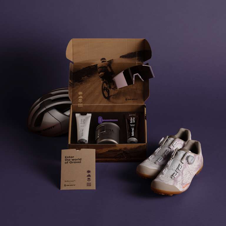 A cycling kit with shoes, helmet, and grooming products is arranged on a purple background, with an open box revealing more items and a scenic cycling image inside.