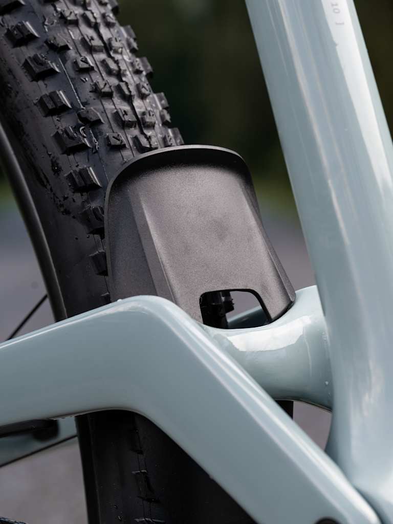 A close-up of a light blue bicycle frame in the foreground is set against a blurred background of trees and a dirt path.