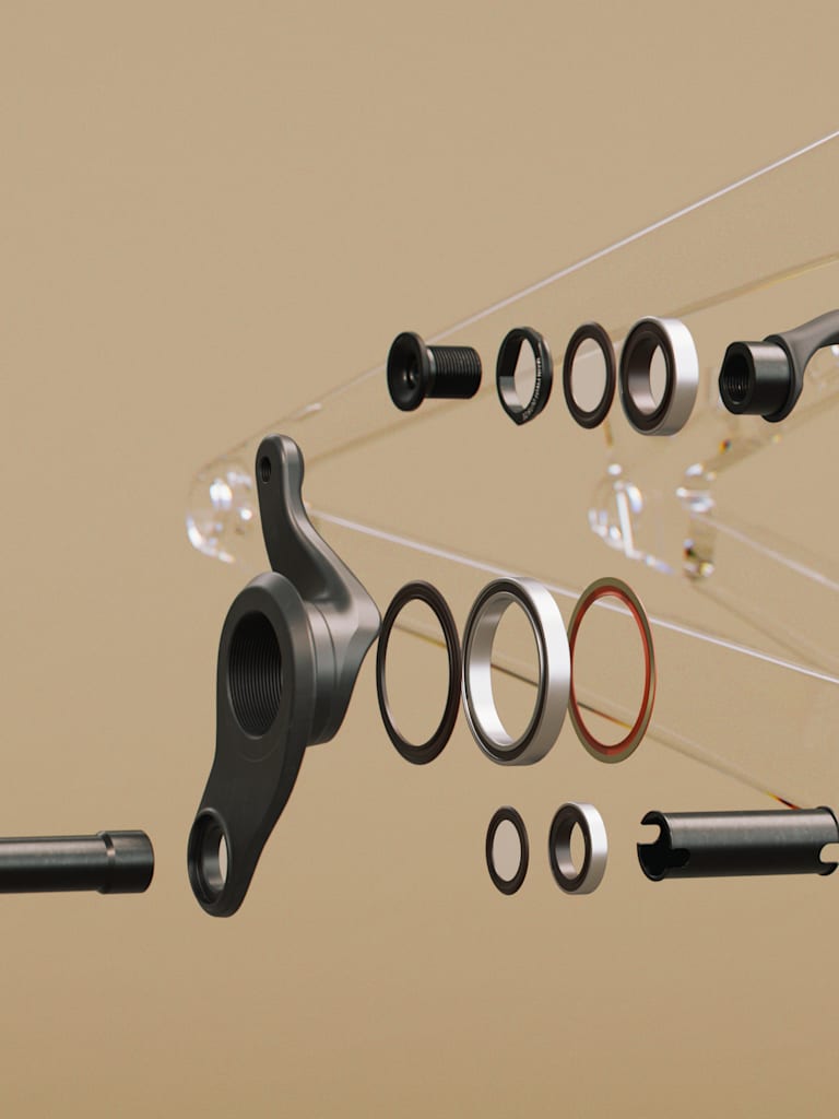 Exploded view of bicycle crankset components in the foreground against a blurred, transparent bicycle frame in the background.