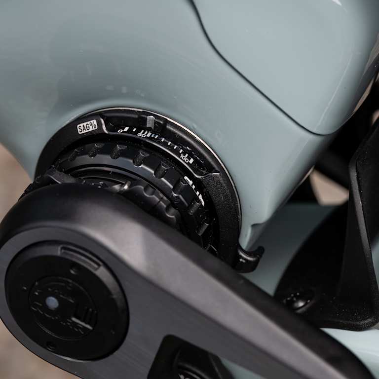 A close-up of a bicycle's crankset and bottom bracket is in the foreground, with the bike's frame and a portion of a tire visible in the background.