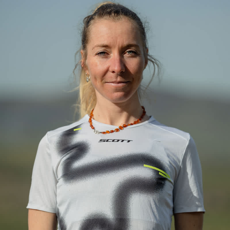 Portrait of Iris Pessey in her SCOTT running shirt, smiling calmly against an open sky