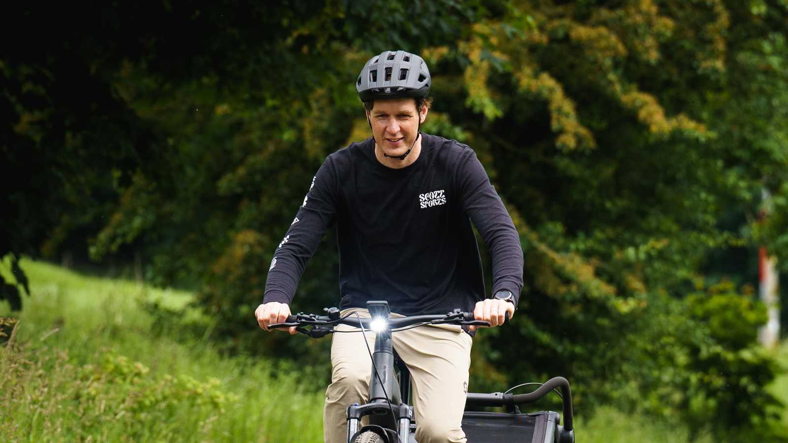Cyclist riding an e-bike with a child trailer on a gravel path