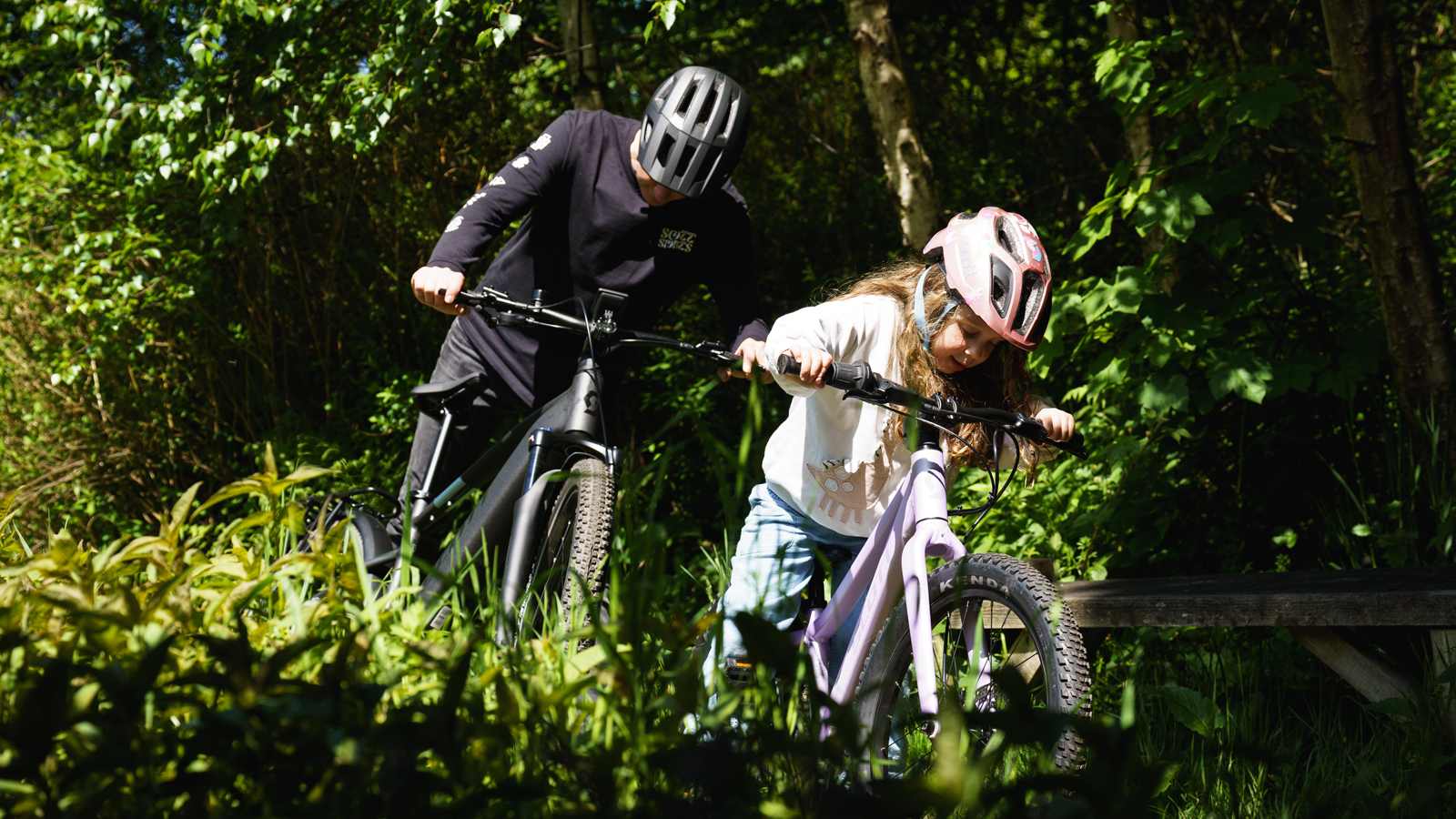 Adult and child riding bikes together on a forest trail