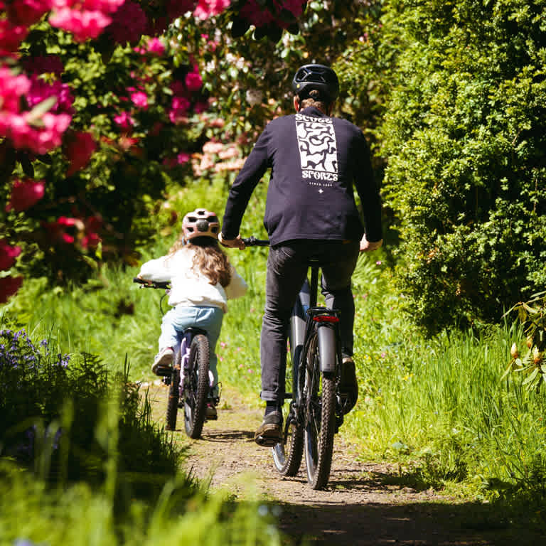 A man and a child riding bicycles together along a scenic path surrounded by greenery.